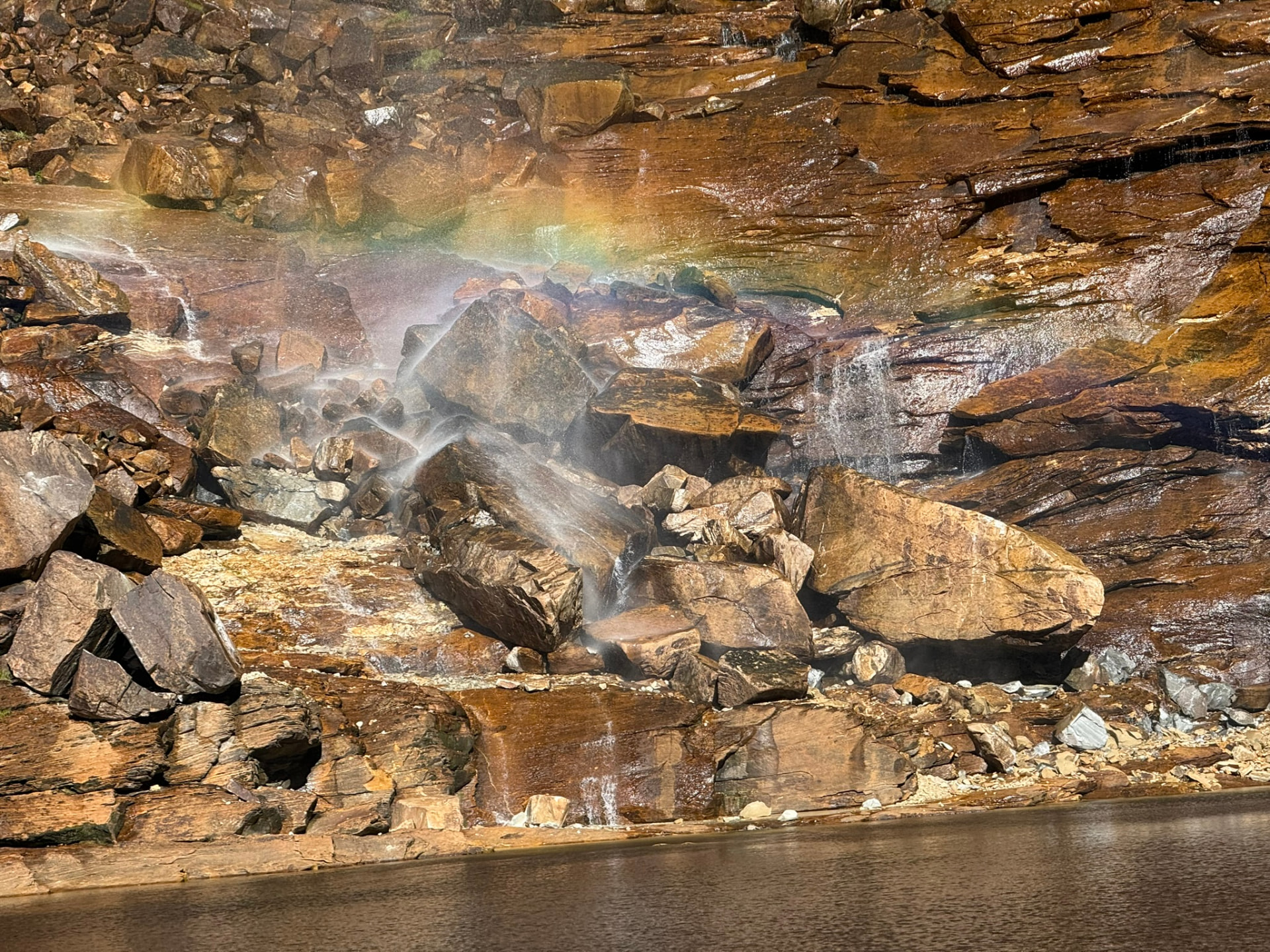 Arco-íris formado pela água que cai entre as rochas da cachoeira