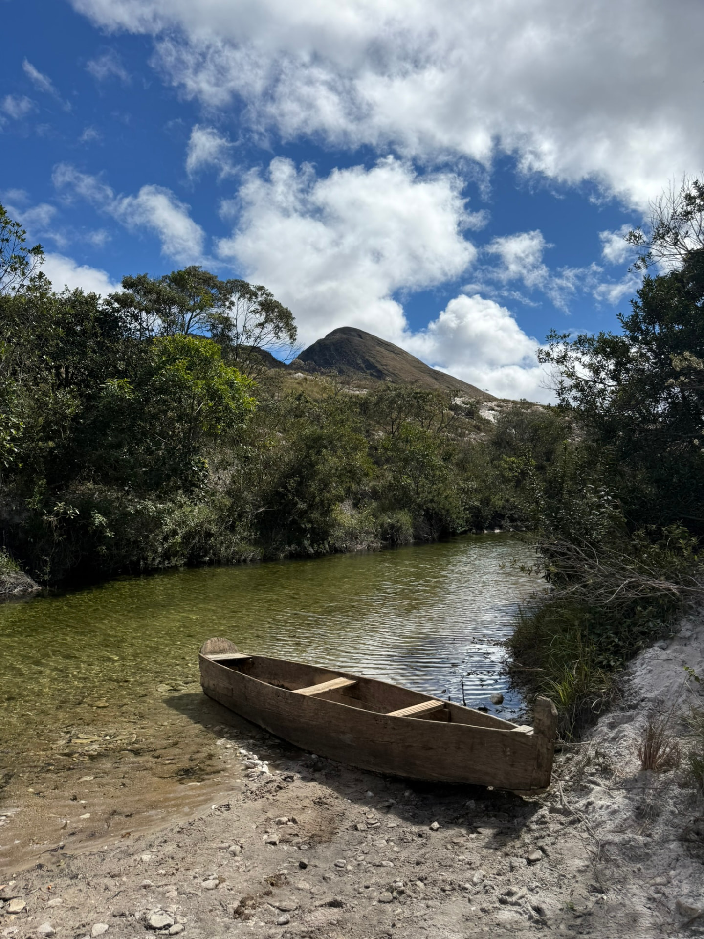 Canoa de madeira à beira de um rio com o pico ao fundo